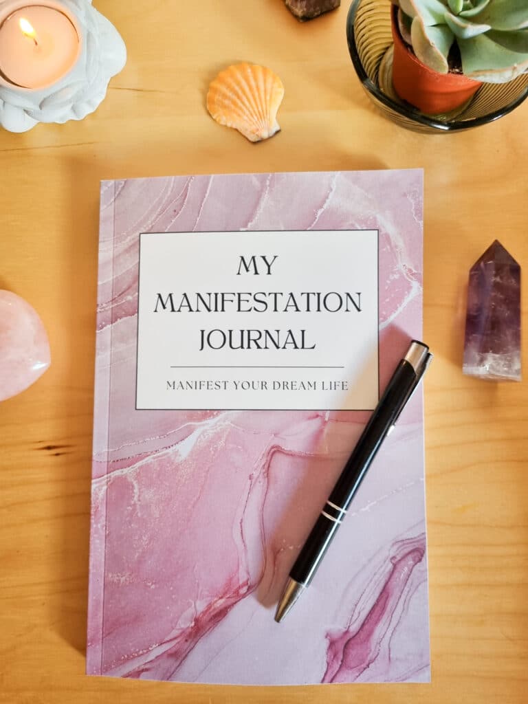 alt="Manifestation Journal with a pen placed on top on a table surrounded by crystals"